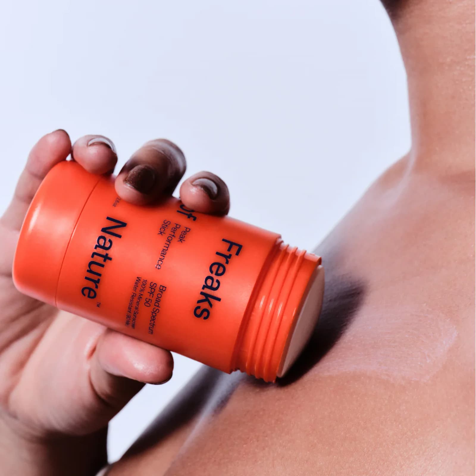 A hand is applying an orange stick of Freaks of Nature Peak Performance stick against their collarbone.