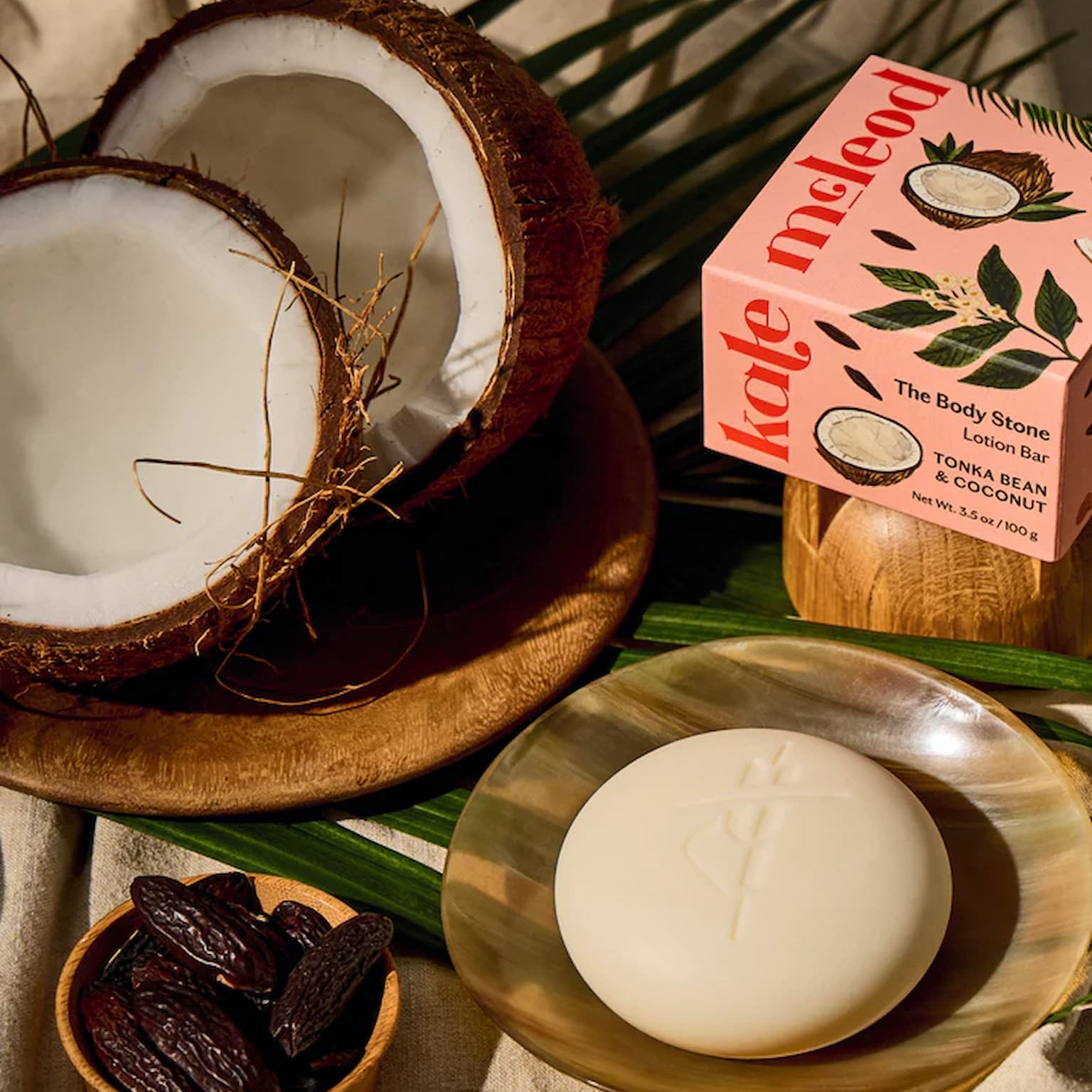 Kate McLeod Body Stone in Limited Edition Tonka Bean & Coconut scent, on a wooden tray with packaging and a coconut.
