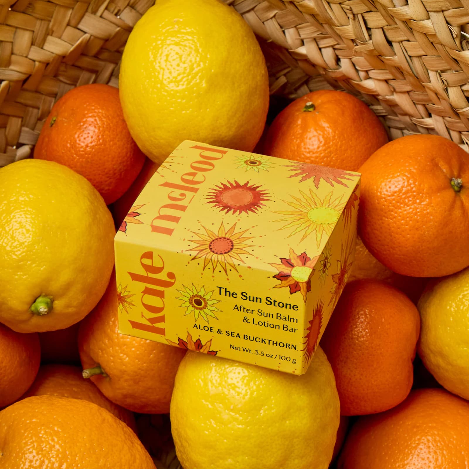 A yellow box of Kate McLeod Sun Stone sits in a brown basket full of oranges and lemons.