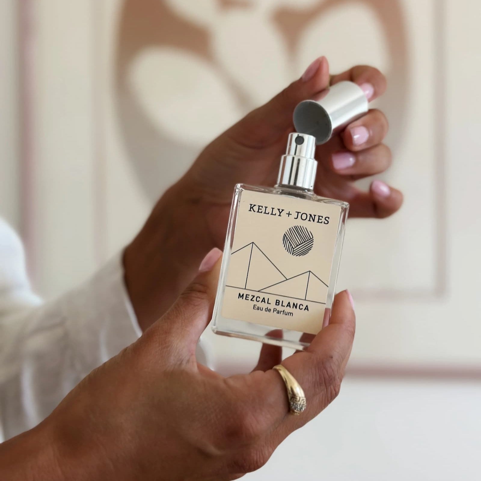 Person holding a Kelly + Jones Mezal Blanca perfume bottle with a decorative background