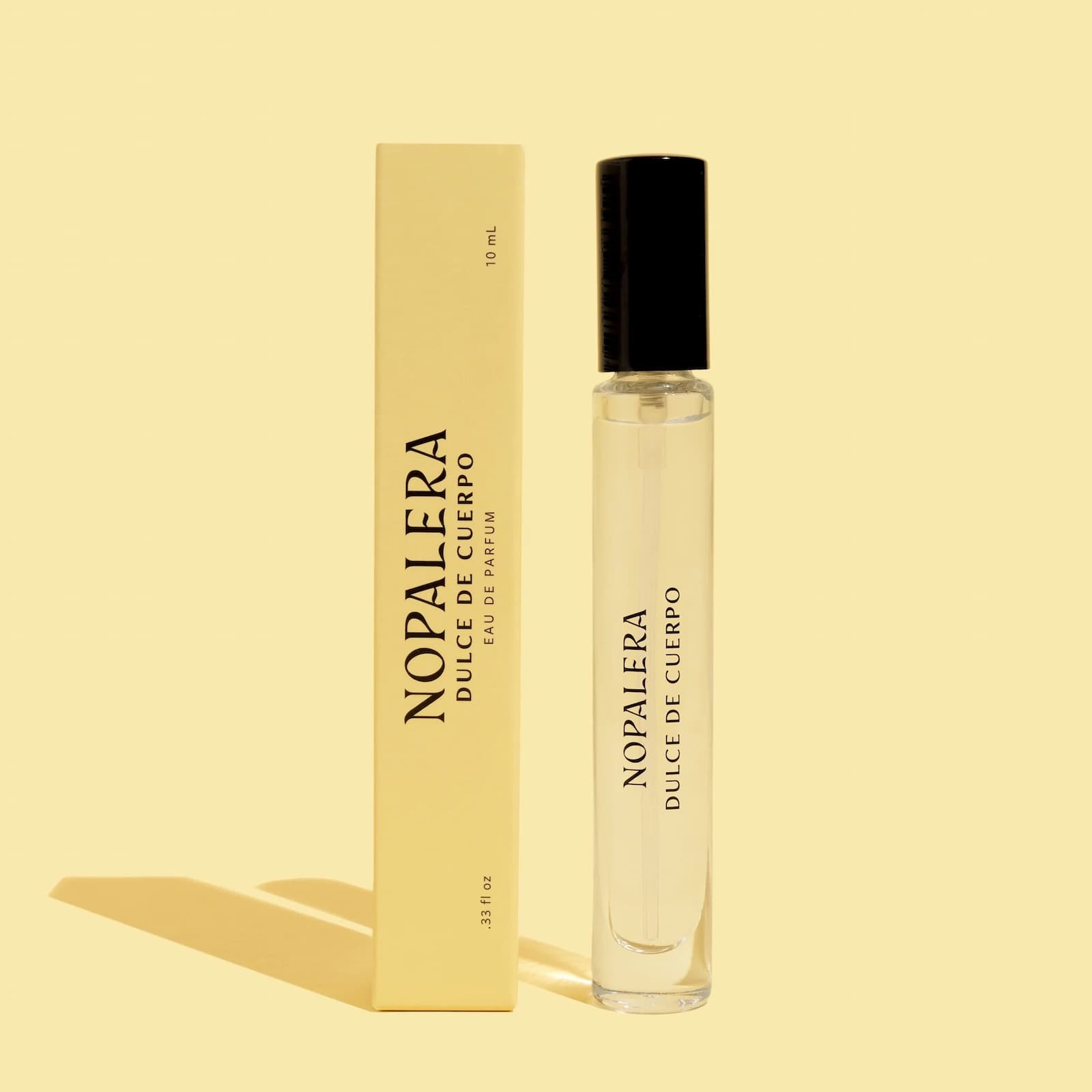 Yellow packaging and glass bottle of the travel size Nopalera Dulce de Cuerpo perfume against a yellow background.