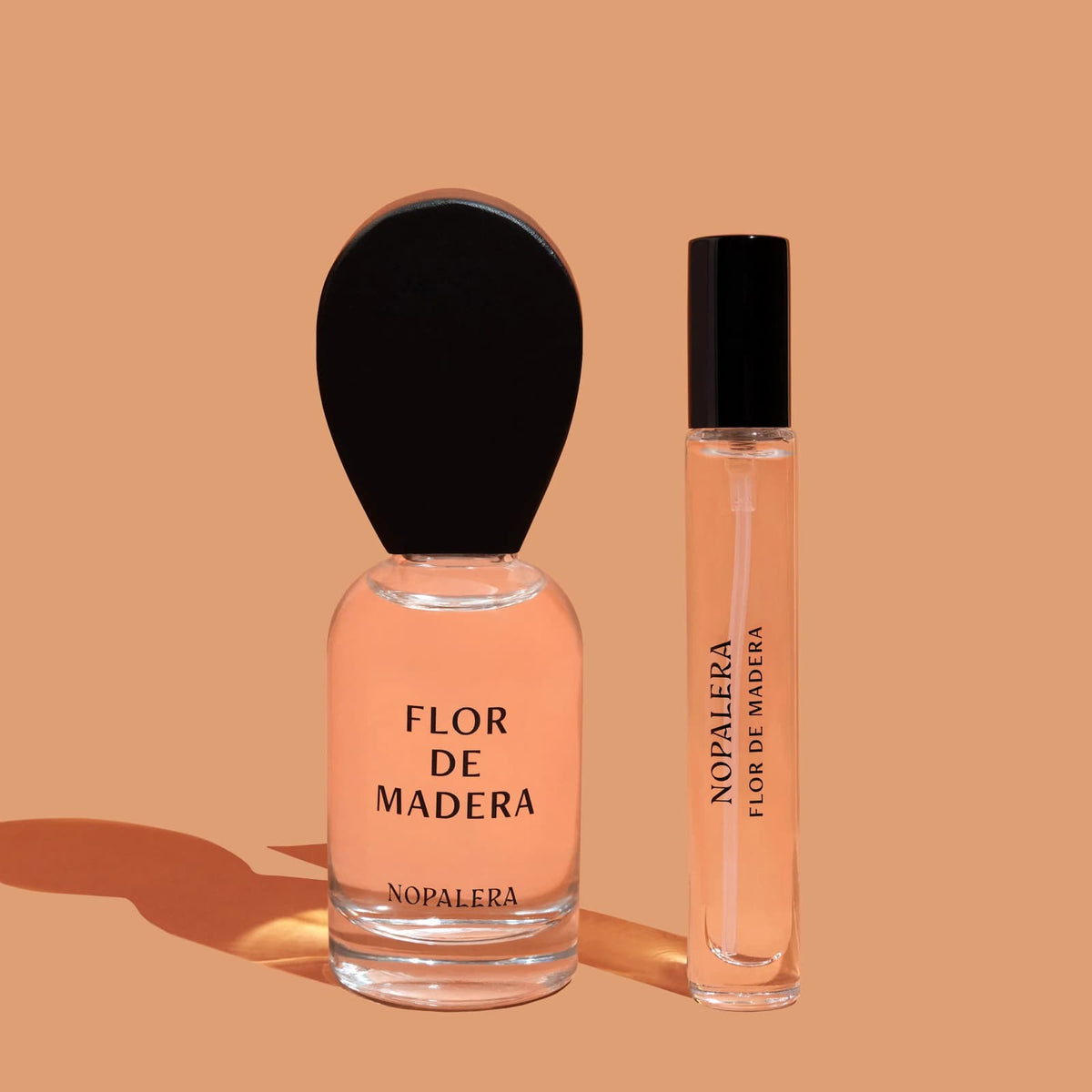 Two glass bottles of Nopalera "Flor de Madera" perfume, one regular and one travel-sized, against an orange background.