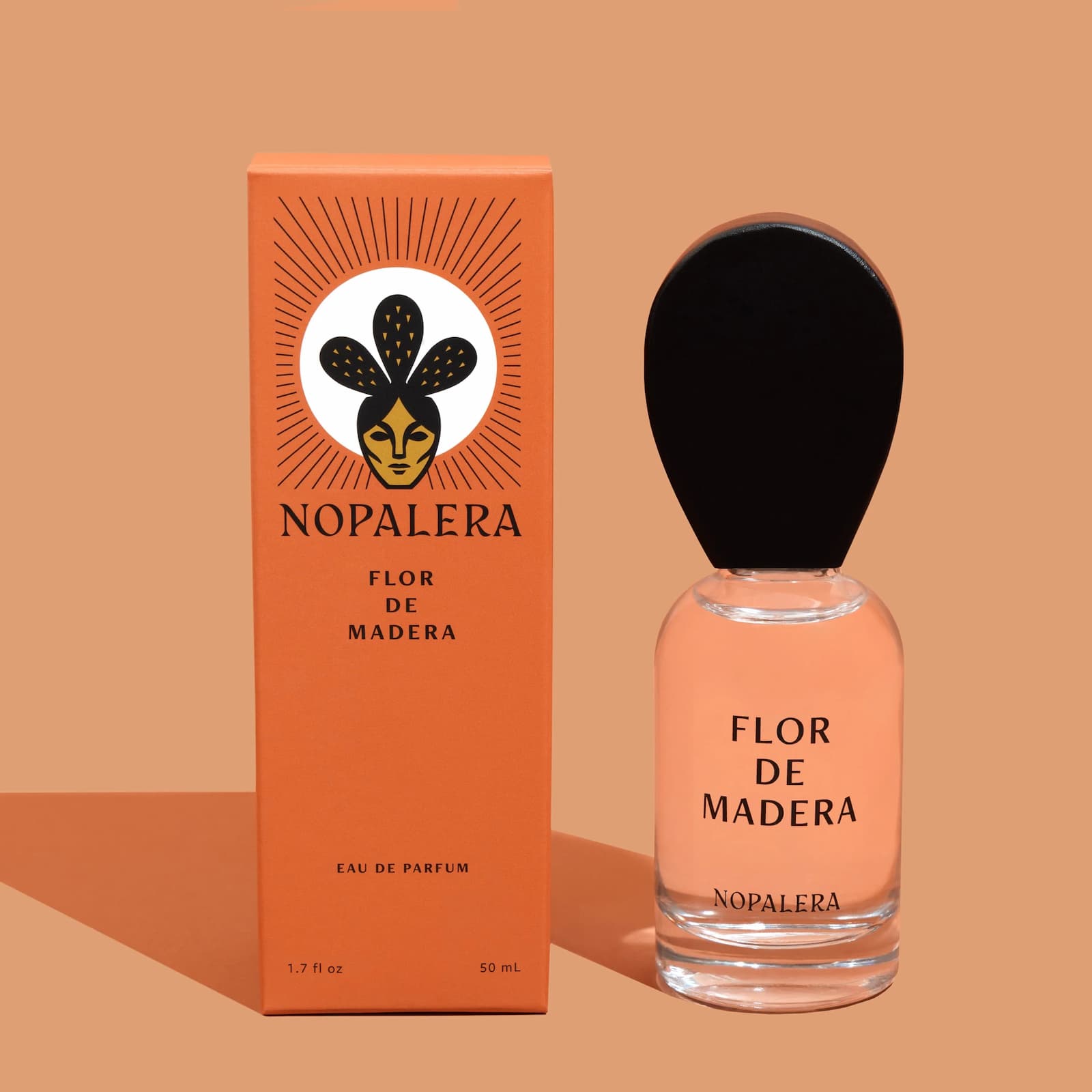 A glass bottle of Nopalera "Flor de Madera" perfume and its orange box against a lighter orange background.