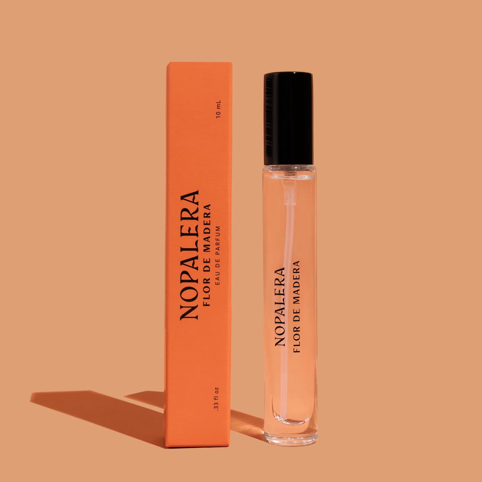 A travel-sized glass bottle of Nopalera "Flor de Madera" perfume and its orange packaging box against a lighter orange background.