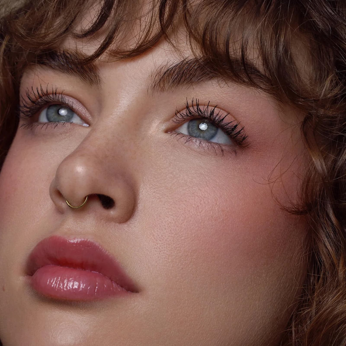 A close-up of a model's face, wearing Rituel de Fille Inner Glow Pigment Balm in "Bee Sting"