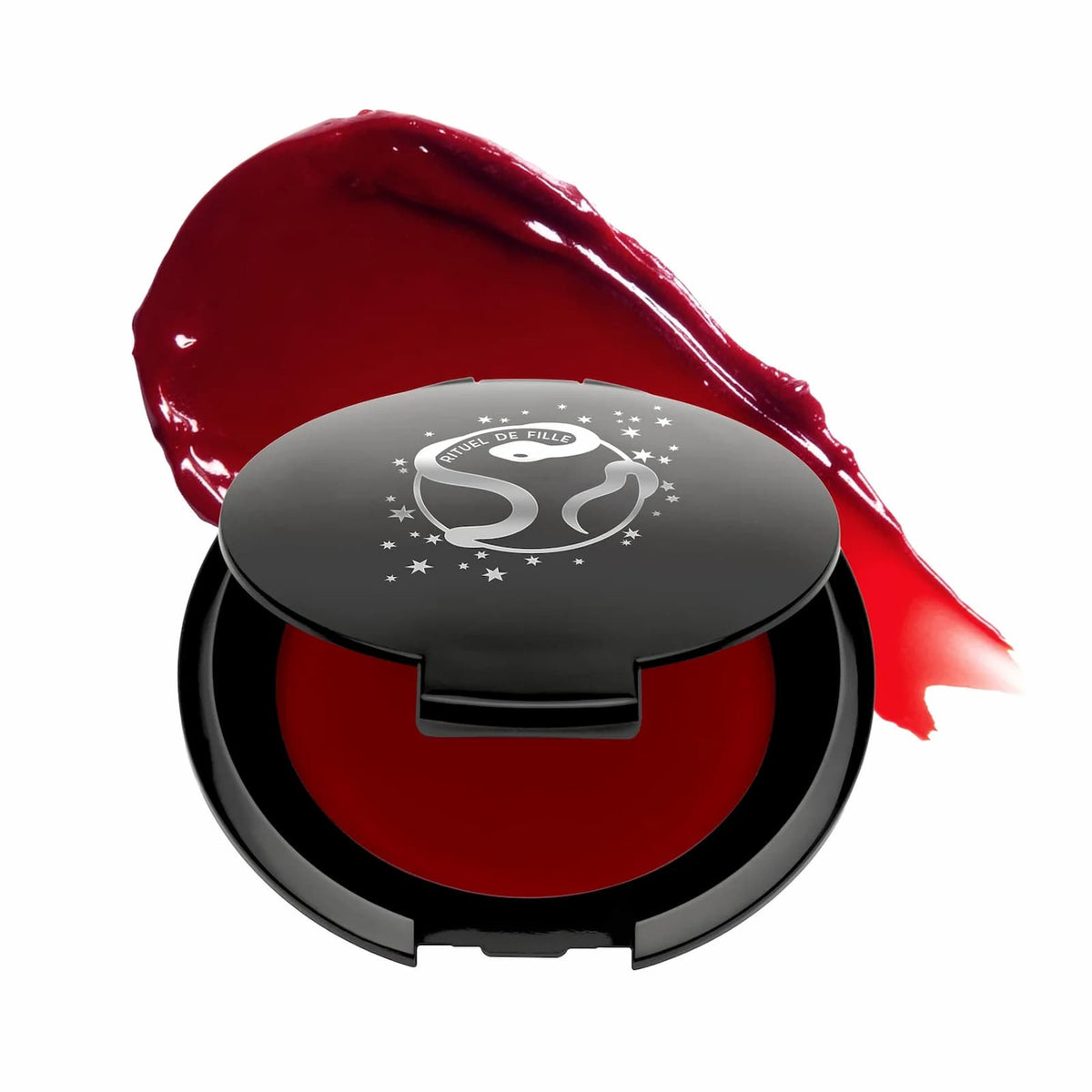 A black makeup compact of Rituel de Fille Inner Glow Pigment Balm in "Bloodflower", with a swatch of product behind it.