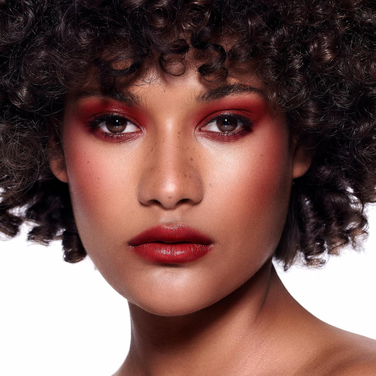A model against a white background, they are wearing Rituel de Fille Inner Glow Pigment Balm in "Bloodflower".