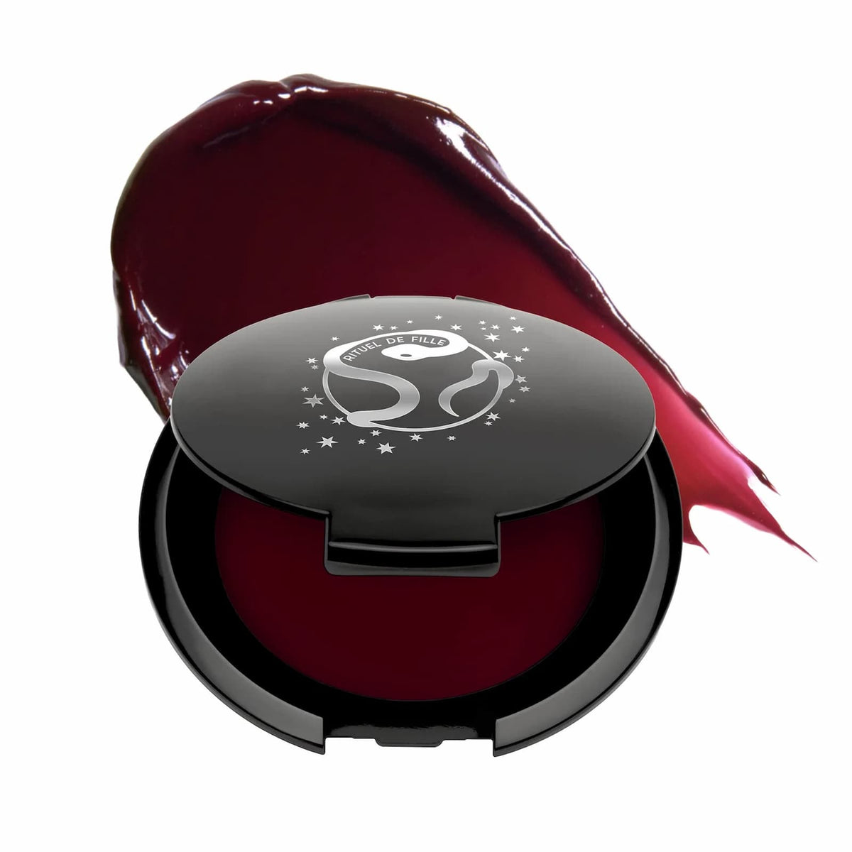 A black makeup compact of Rituel de Fille Inner Glow Pigment Balm in "Weeping Cherry", with a swatch of product behind.
