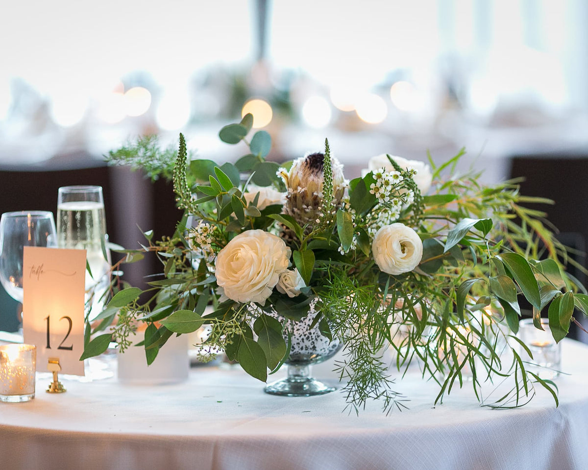 Roundhouse wedding reception with decorative floral arrangement on a table with candles and a number card in a blurred indoor setting.