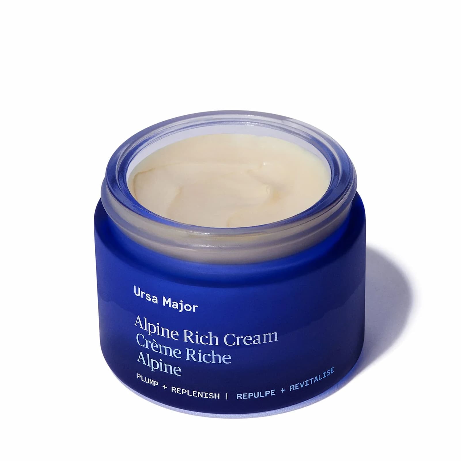 An open dark blue jar of Ursa Major Alpine Rich Cream. The product is an off-white color.
