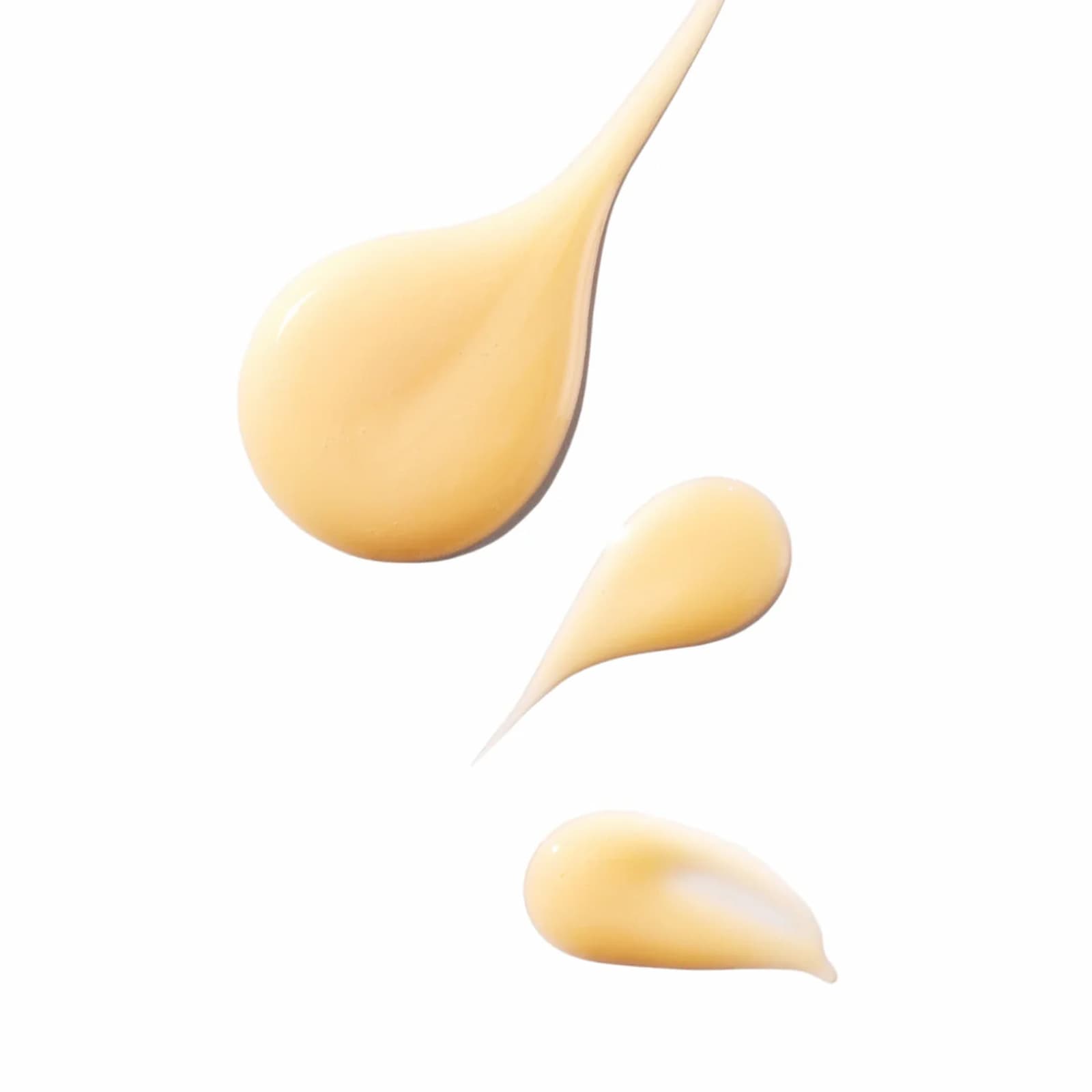 Three slightly yellow teardrop-shaped dollops of Ursa Major Brighten Up Vitamin C Serum on a white background.